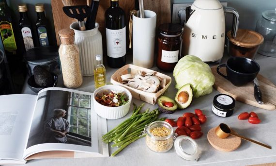Various colorful healthy food and vegetables locating on countertop next to many different utensils and white kettle during cooking in stylish kitchen